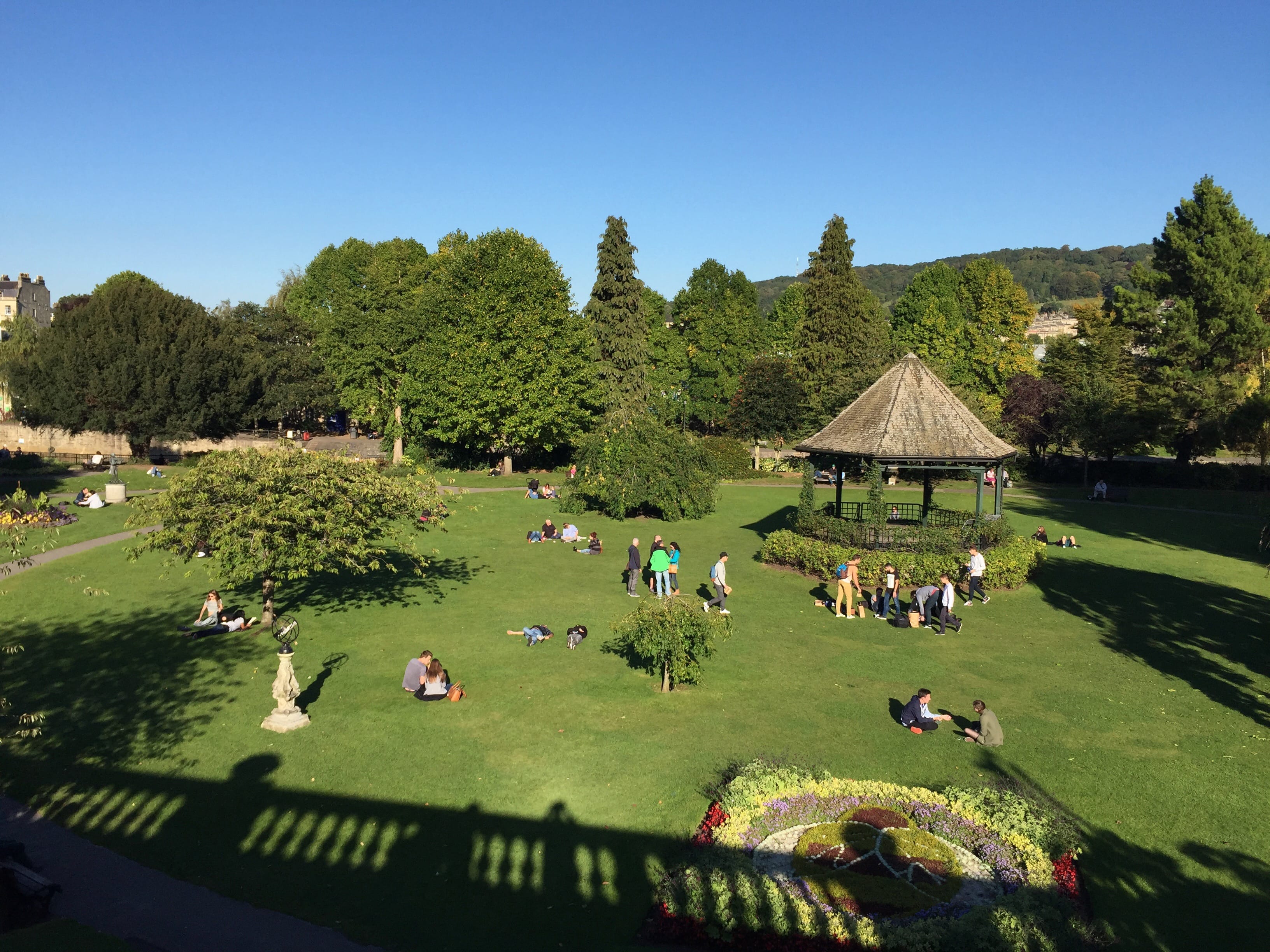 Parade Gardens park with green grass, trees, a gazebo and people sitting on the grass.