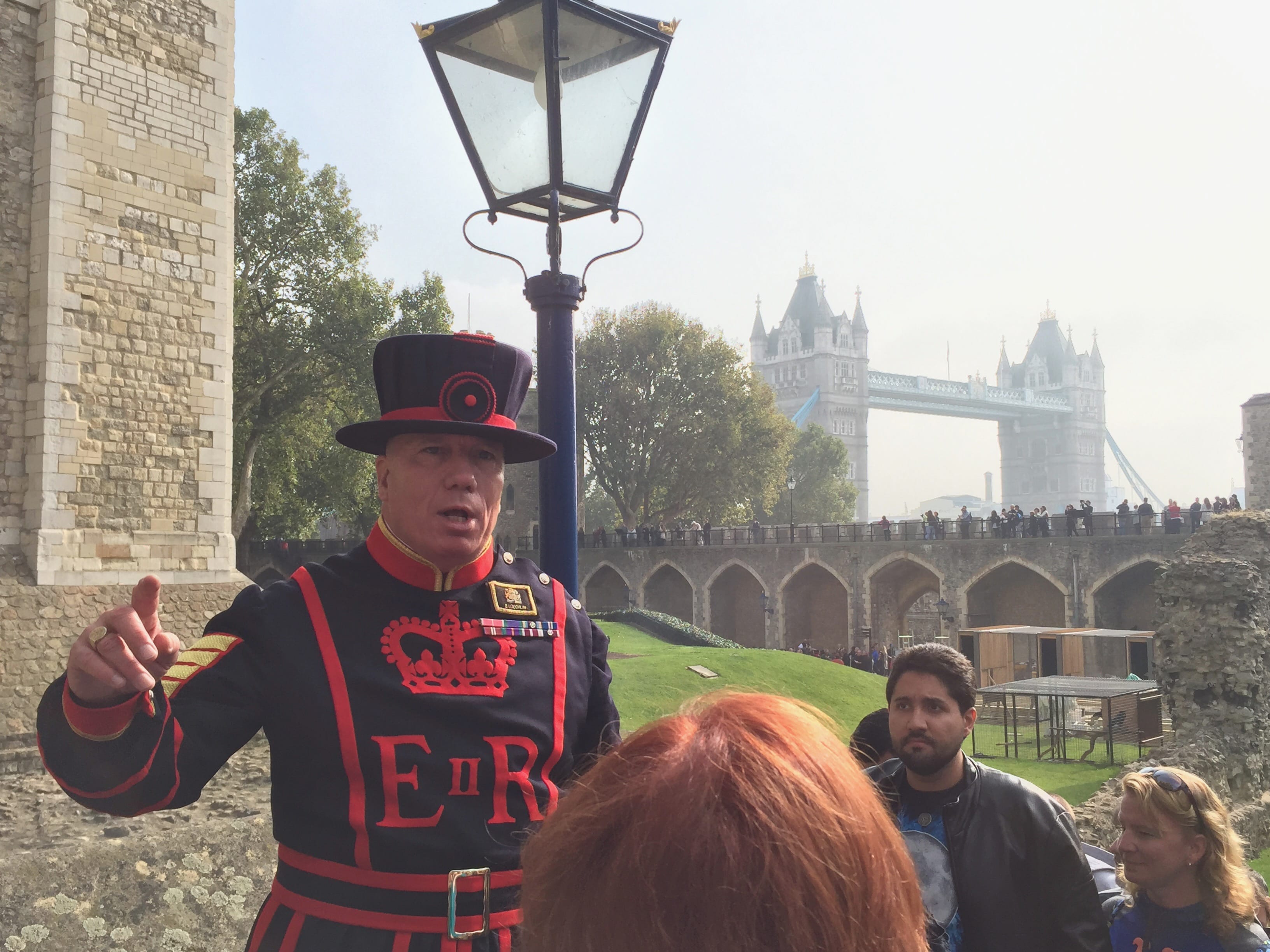 A Royal Gaurd member in traditional dress explaining abotu the Tower of London with Tower Bridge in the background.