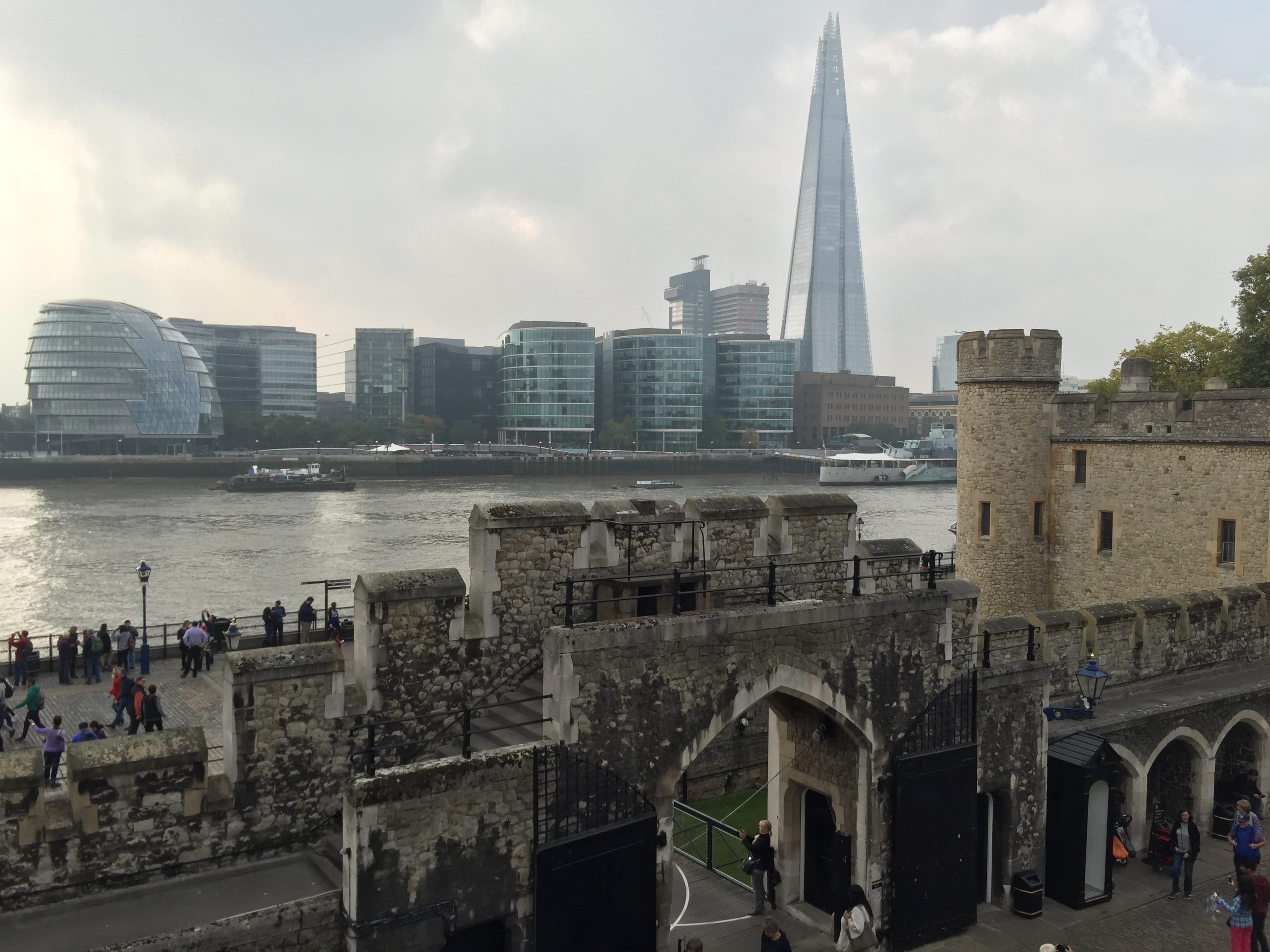 A view toward the river thames from the Tower of London, with the old brick walls in the foreground and modern city across the river in the background.