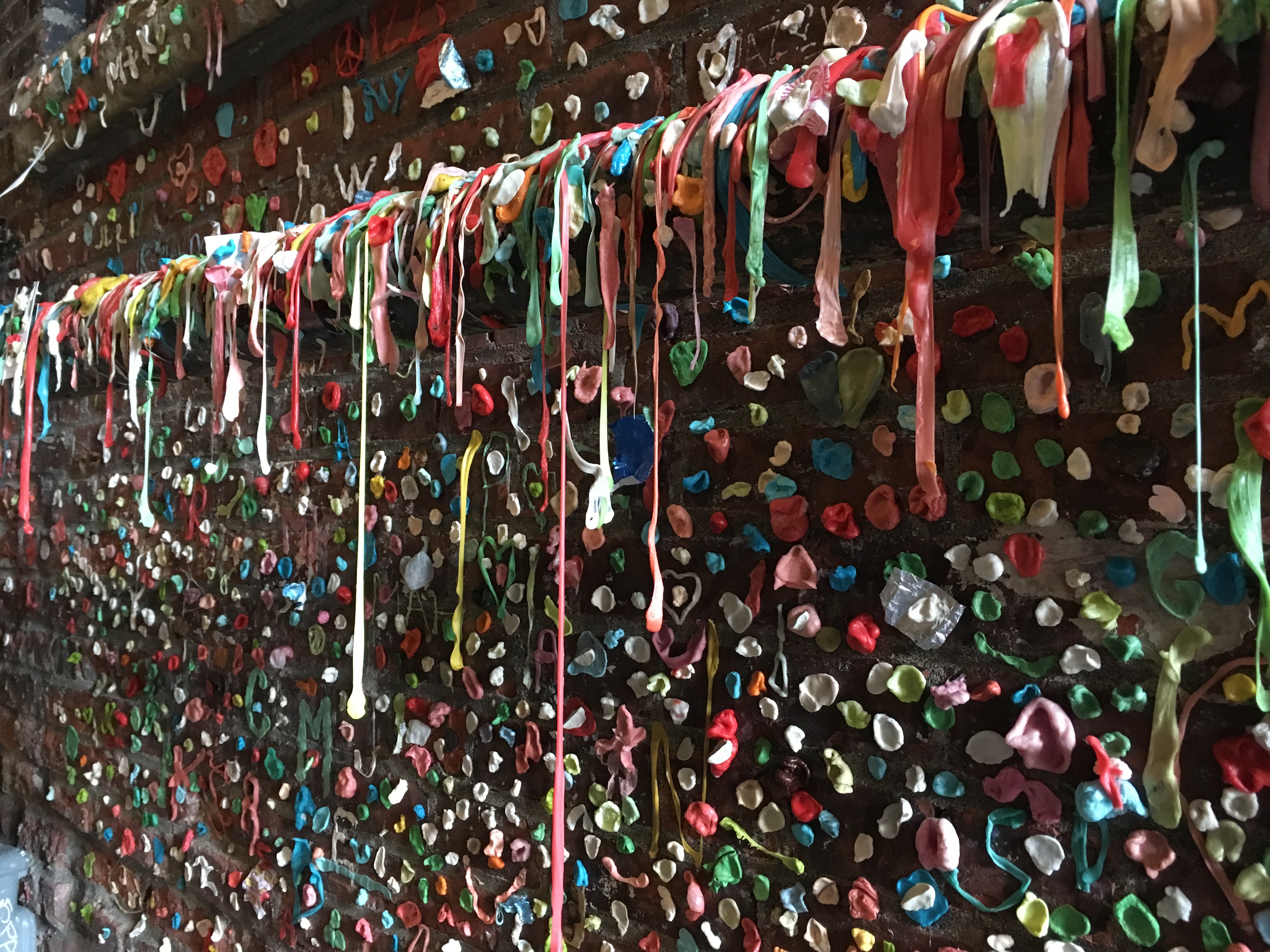 A close up shot of a wall covered in chewed up bubble gum. There is a ledge where gum is pulled down to look like it's dripping over the edge.