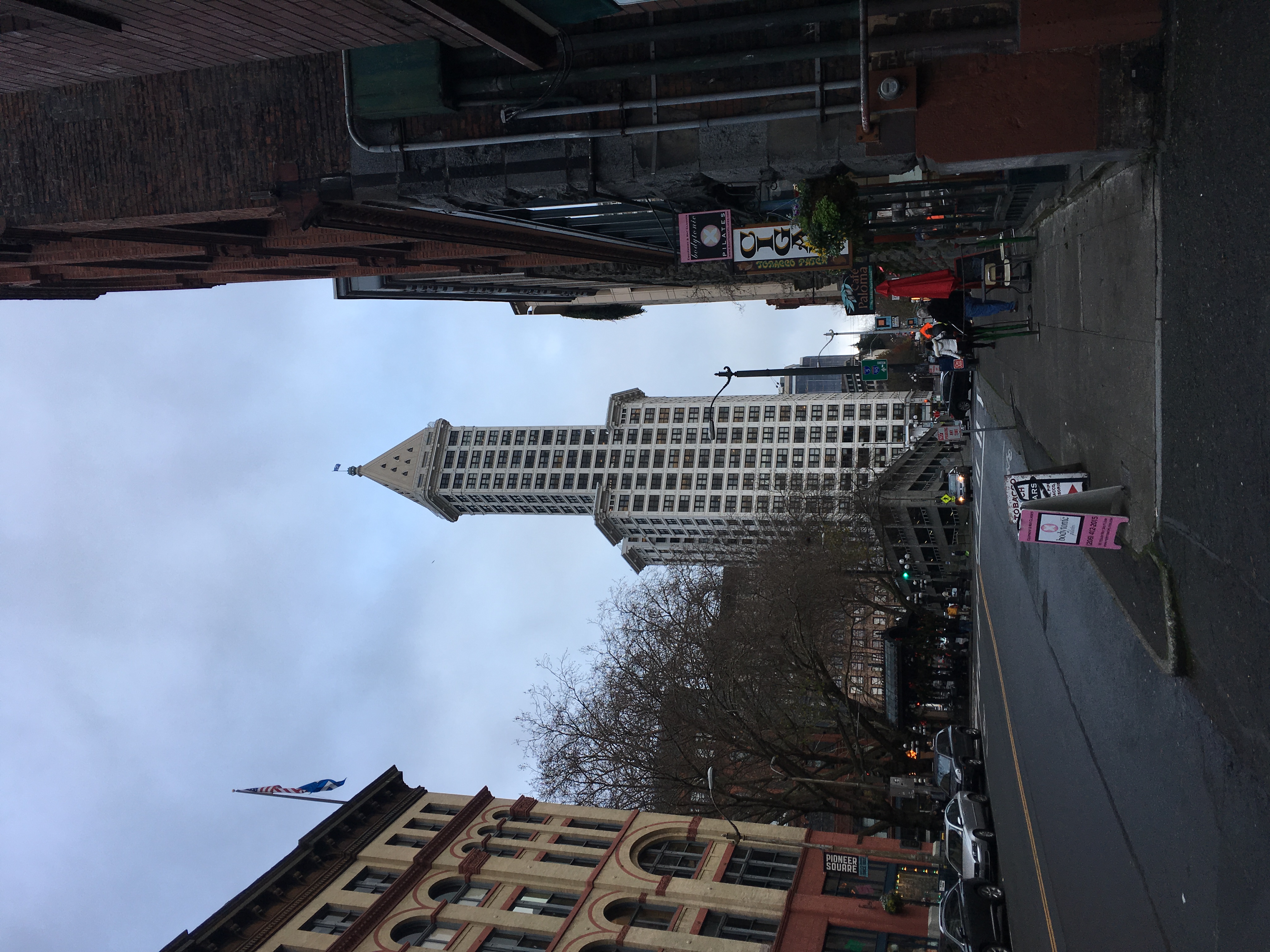 A view down a street with buildings on each side, with Smith Tower in the center of the image. Smith Tower is a tall ivory building with a pyramid at the top.